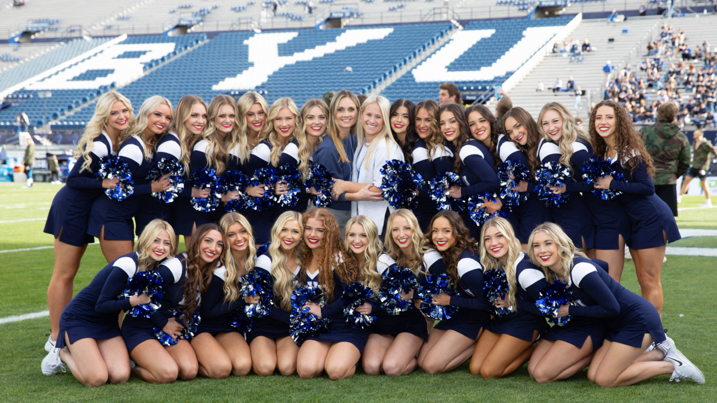 BYU Cougarettes on the football field posed before the game starts with BYU seats in the background